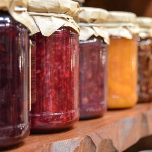 A close-up view of various homemade jam jars lined up on a wooden shelf.