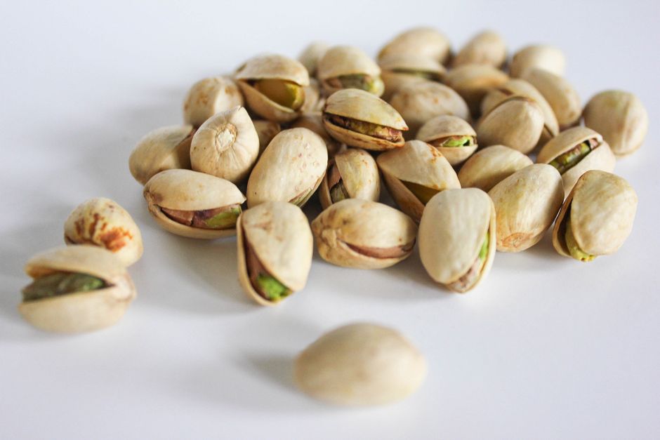 A close-up image showcasing a pile of fresh pistachios with their shells on a white surface. Perfect for food themes.