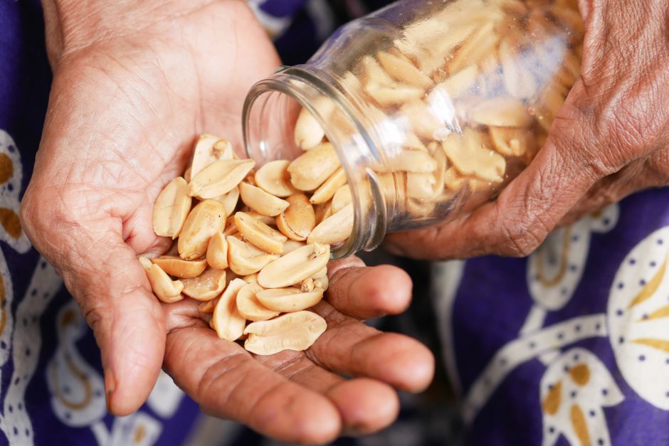 Close-up of elderly hands pouring roasted peanuts from a glass jar into a palm.