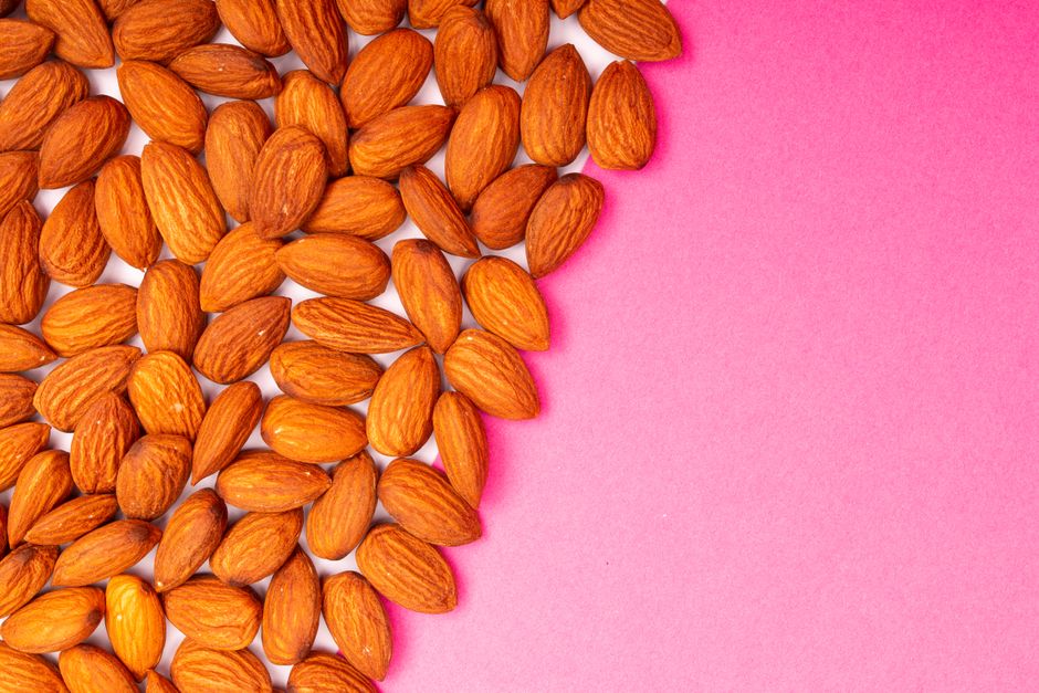 A flatlay of nutritious organic almonds scattered on a vibrant pink surface with ample copy space.
